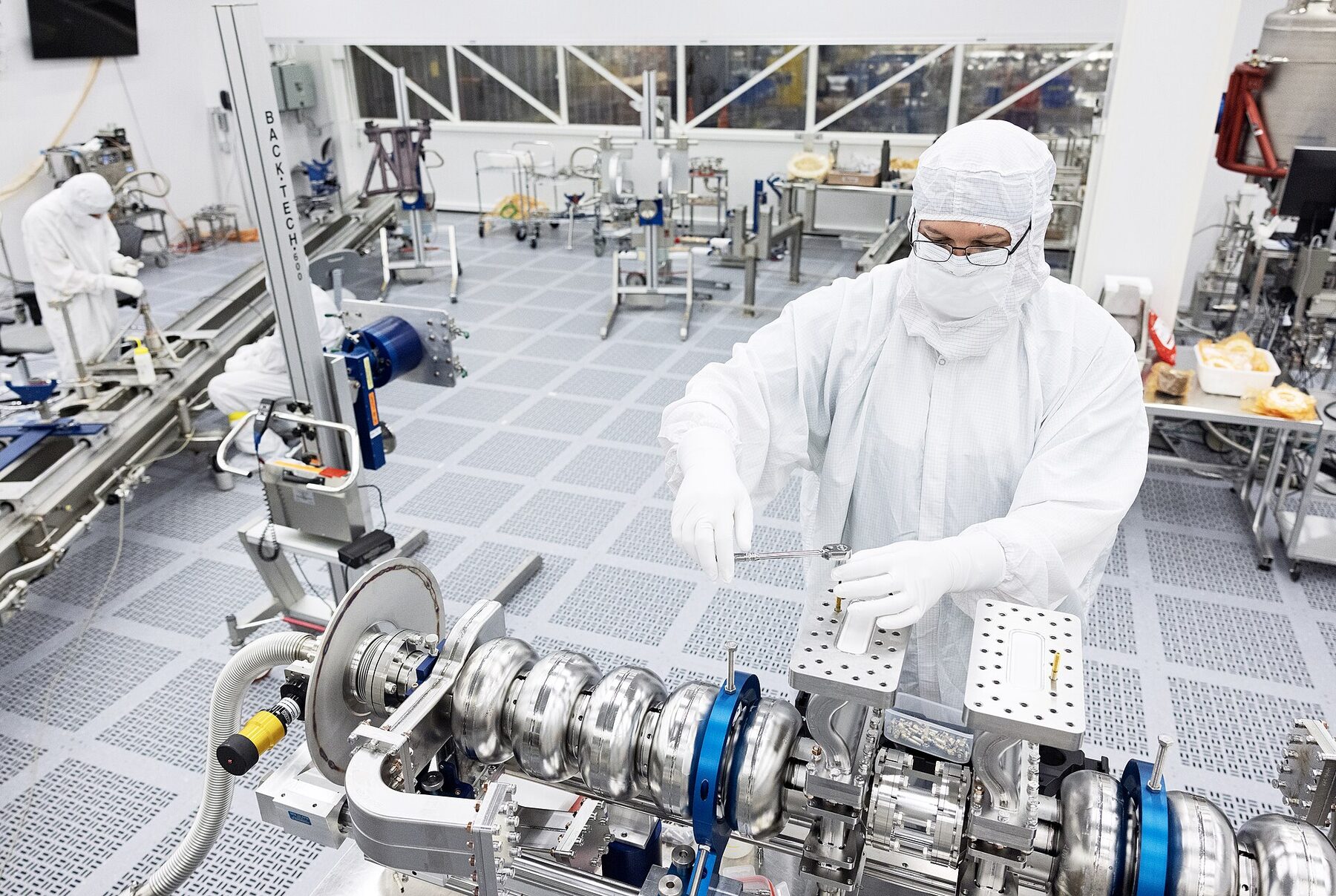 Technicians in clean-room clothing working on precision equipment
